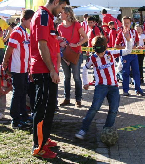 Un niño aficionado del Atlético de Madrid con un antifaz prueba a jugar con el balón