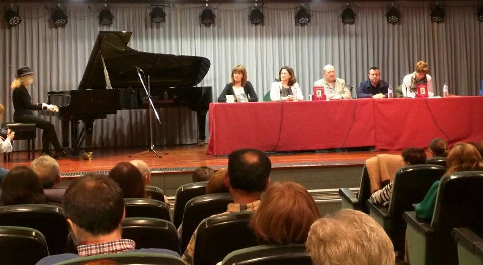 Todos los participantes en la presentación escuchan desde la mesa a Carolina Loureiro al piano