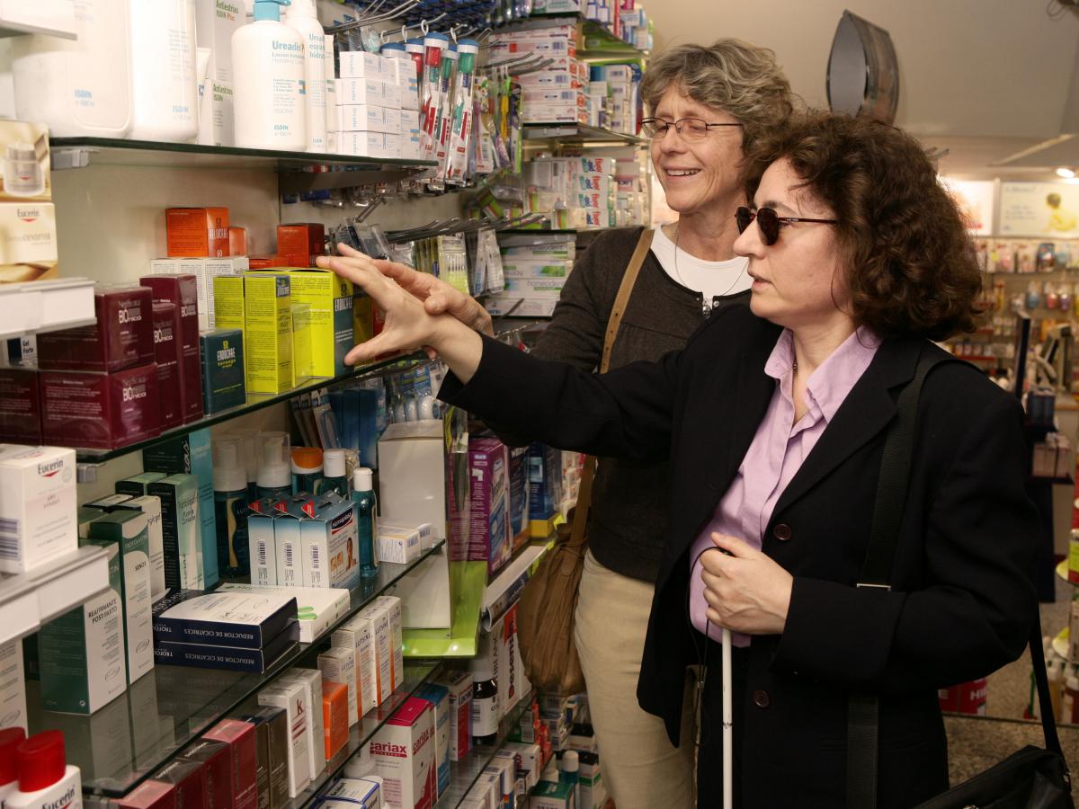 Una voluntaria acompaña a una afiliada a realizar sus compras en una farmacia