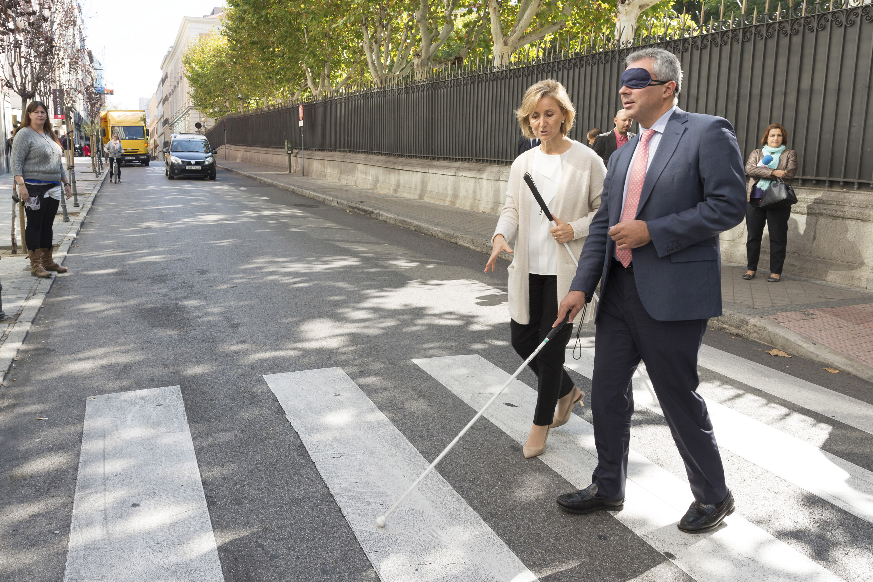 el_consejero_carlos_izquierdo_cruza_una_calle_con_un_antifaz_y_un_baston_blanco_ayudado_por_una_tecnico_de_rehabilitacion_de_la_once.jpg